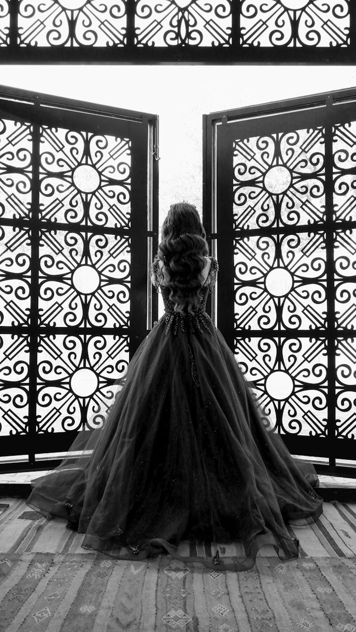 A woman in a black dress stands elegantly before decorative doors, embodying grace and sophistication.