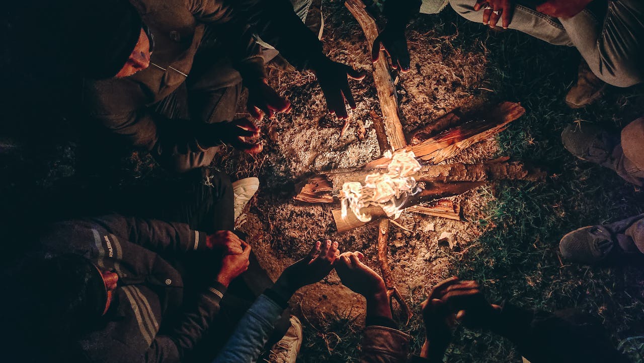 A group of adults warming hands by a campfire at night in India.